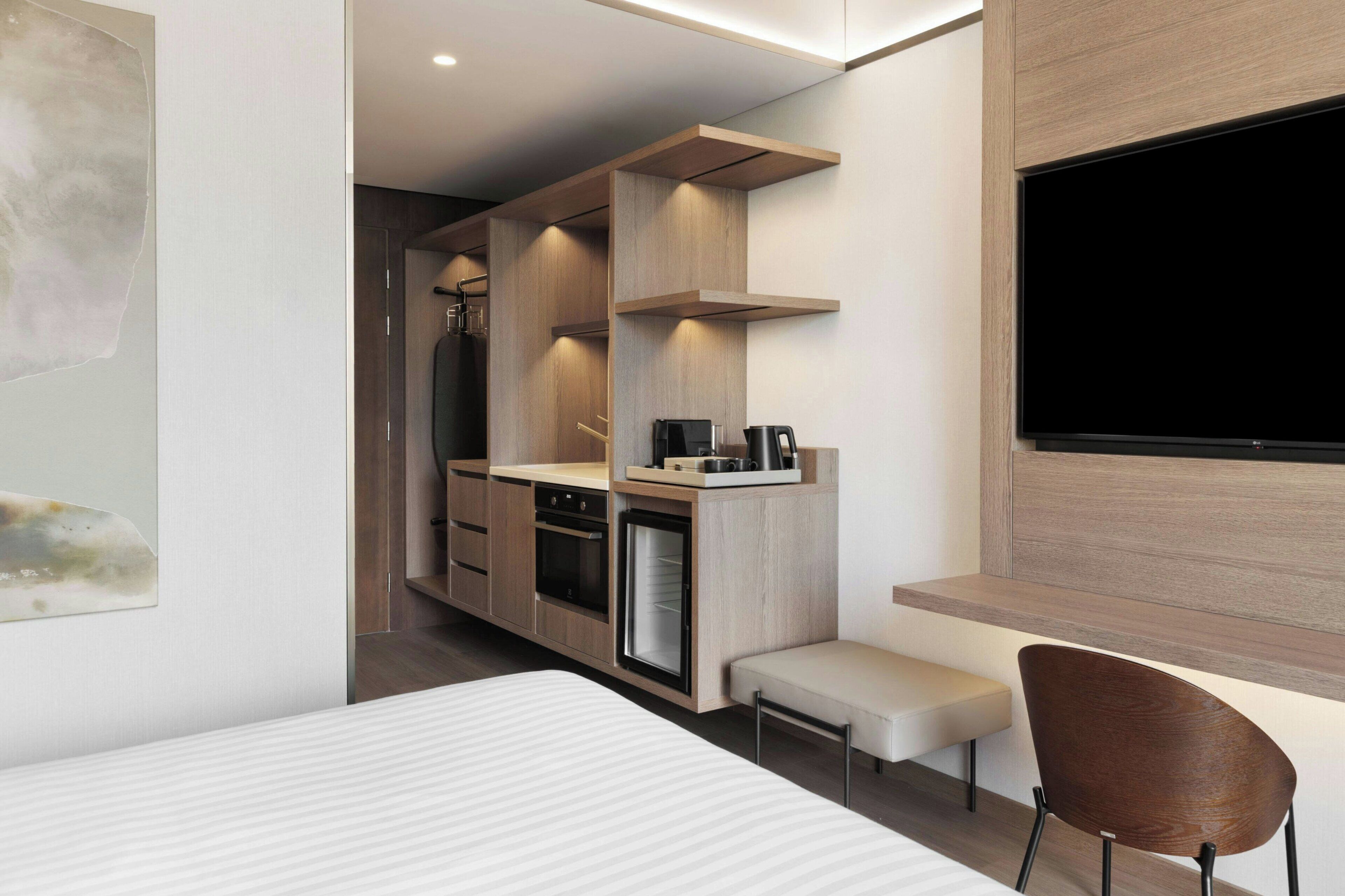 A modern hotel room with a kitchenette, a flat-screen TV, a bed, and a seating area.