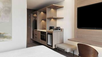 A modern hotel room with a kitchenette, a flat-screen TV, a bed, and a seating area.