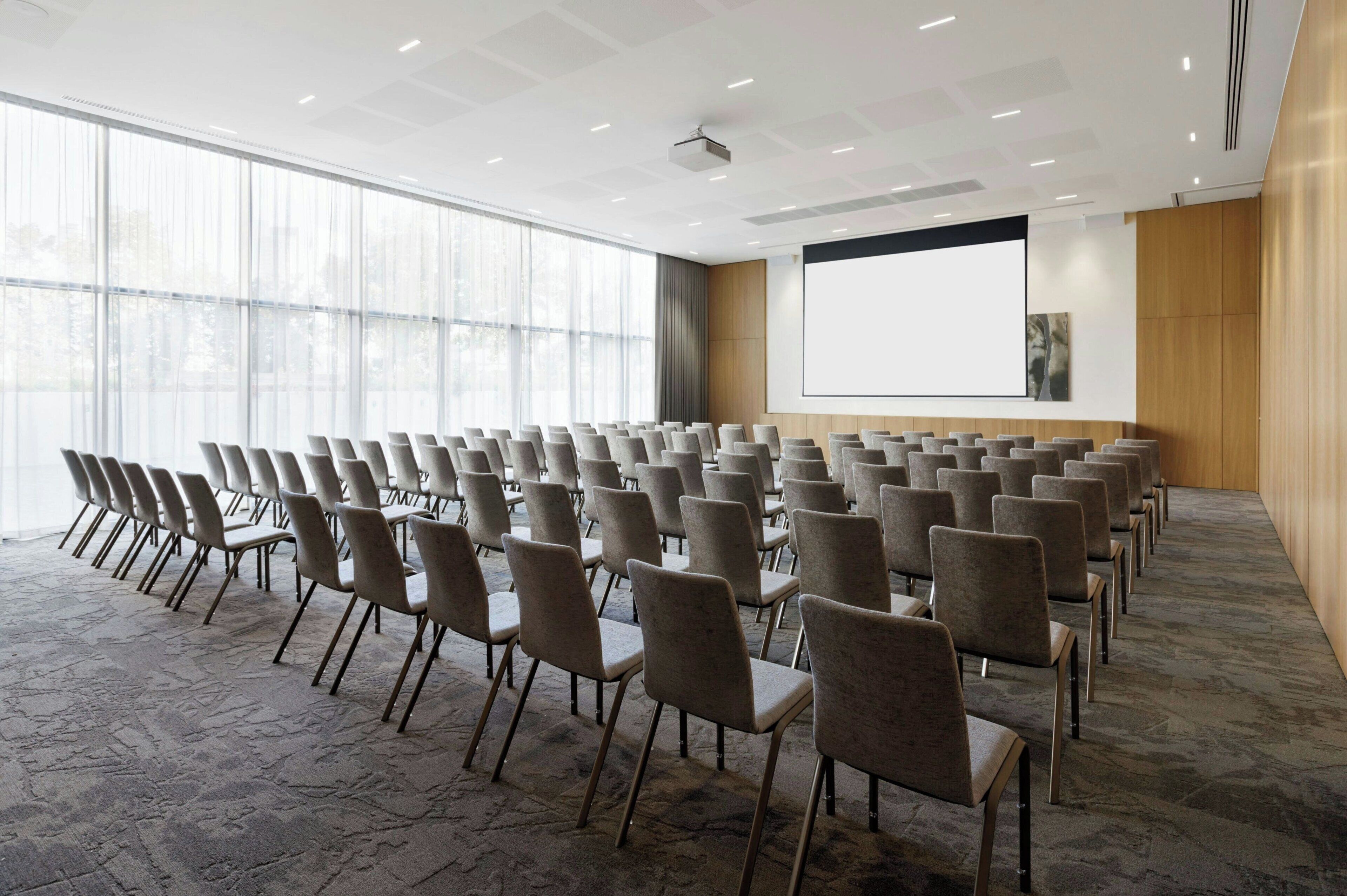 Una sala conferenze con file di sedie, un grande schermo e un proiettore.