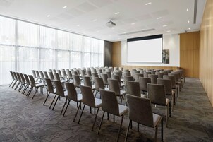 Una sala conferenze con file di sedie, un grande schermo e un proiettore.
