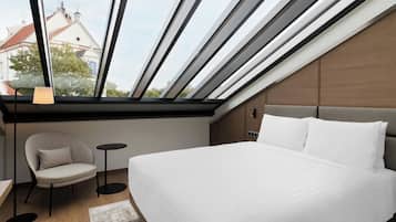 Un dormitorio moderno con tragaluz, una cama, una silla y una mesita.