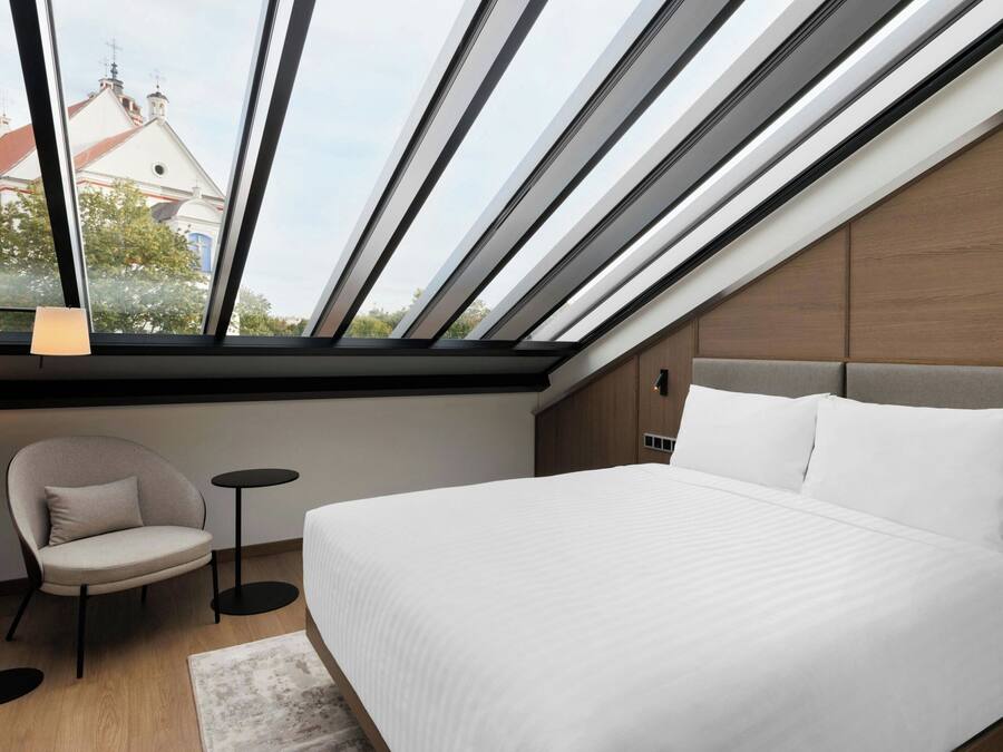 Un dormitorio moderno con tragaluz, una cama, una silla y una mesita.