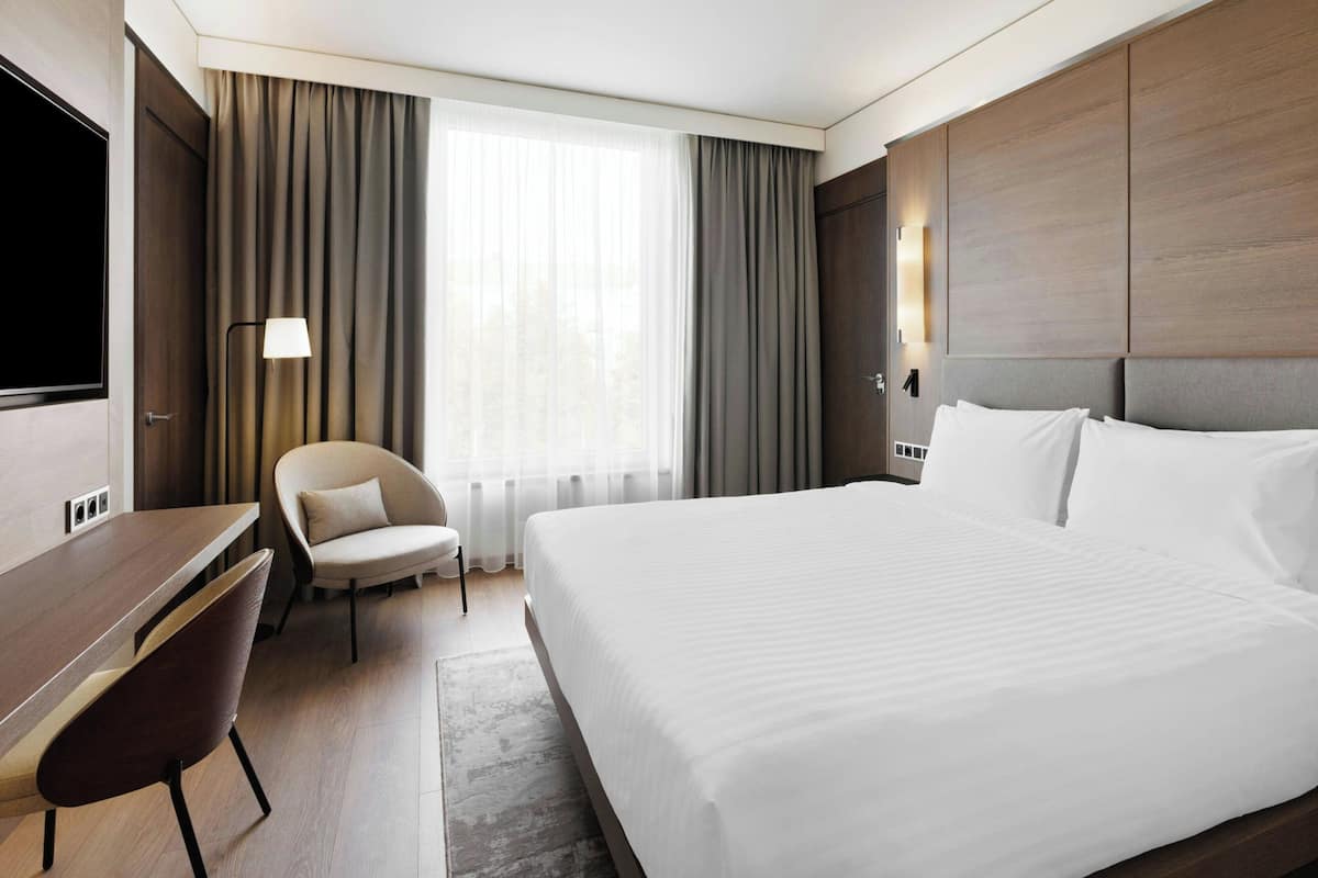 Ett hotellrum med en stor säng, ett skrivbord, en stol och en tv.