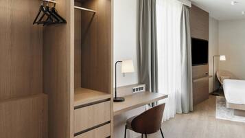 Quarto de hotel moderno com guarda-roupa de madeira, uma escrivaninha com luminária, uma cama e uma televisão.