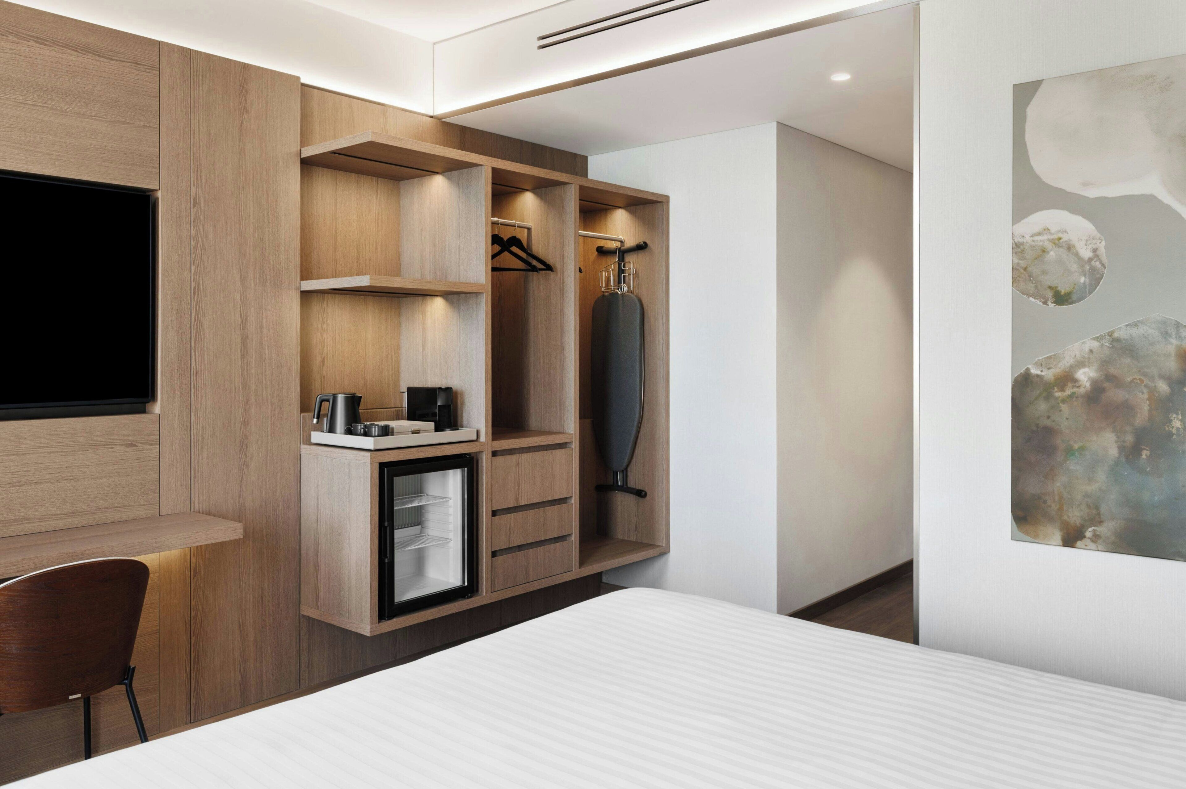Una habitación de hotel moderna con armario empotrado, kitchenette pequeña y una cama.