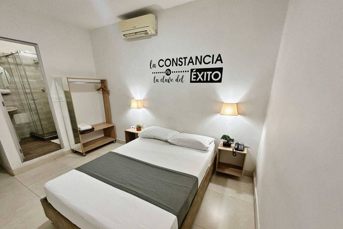 A modern hotel room with a bed, bedside tables, a mirror, a shower, and a wall with motivational text.
