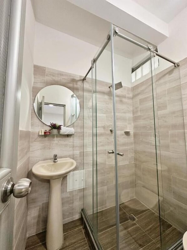 Un baño moderno con cabina de ducha de vidrio, un lavabo sobre pedestal y un espejo encima.