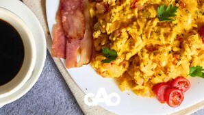 A plate with scrambled eggs, bacon, and a side of sliced tomatoes, accompanied by a cup of coffee and a bowl of sauce. - Hotel Boutique Gao (San Jose de Cucuta)