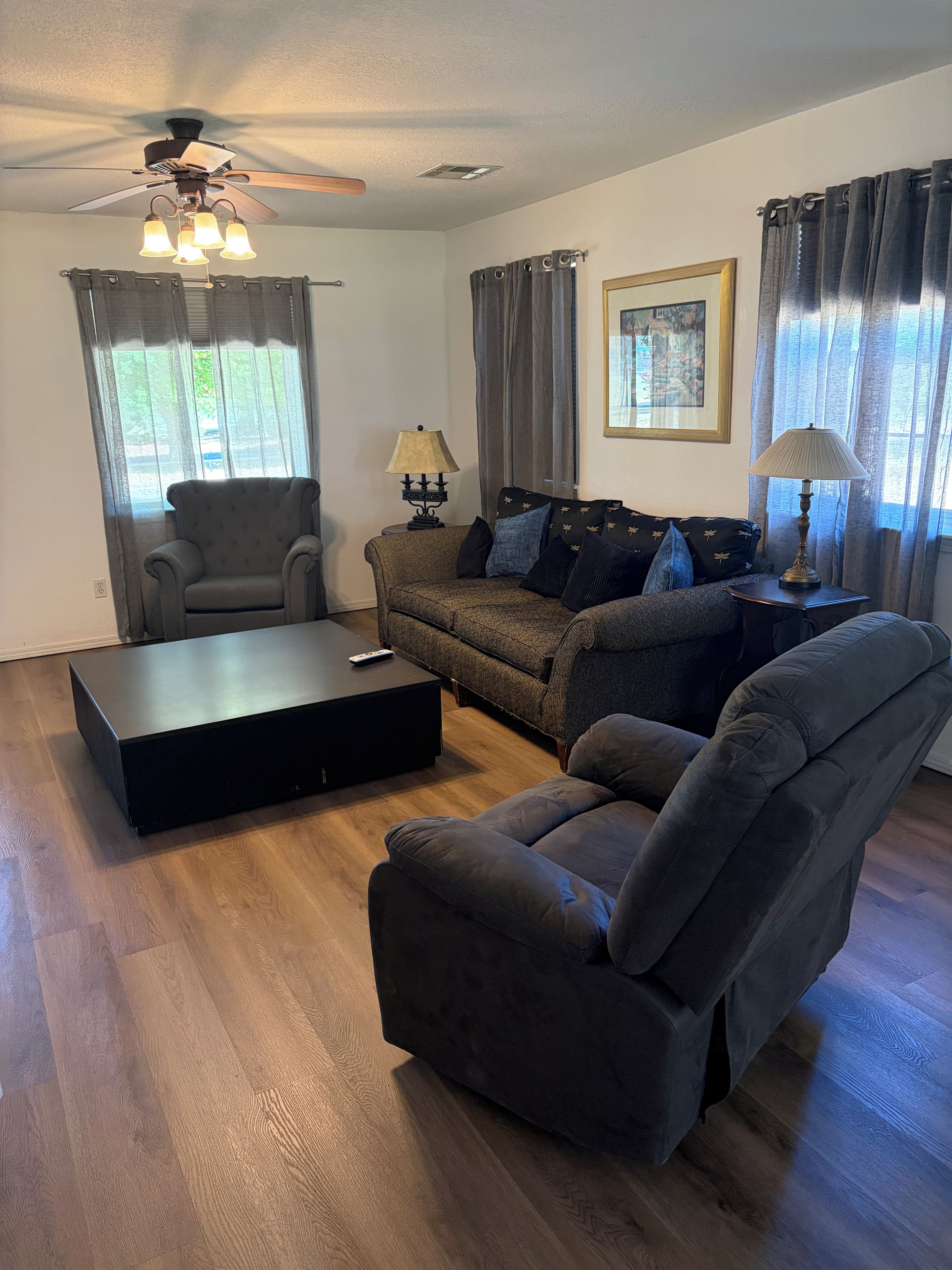 Una sala de estar con sofá, sillón, mesa de centro y ventilador de techo.