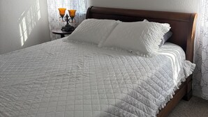 A neatly made bed with a quilted white duvet, a wooden headboard, and two framed pictures on the wall. - Charming 3-bedroom house . Across the street from a beautiful walking track (McAlester)
