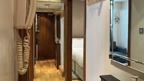 A hotel hallway with wooden flooring, a coat rack, a mirror, and a phone.