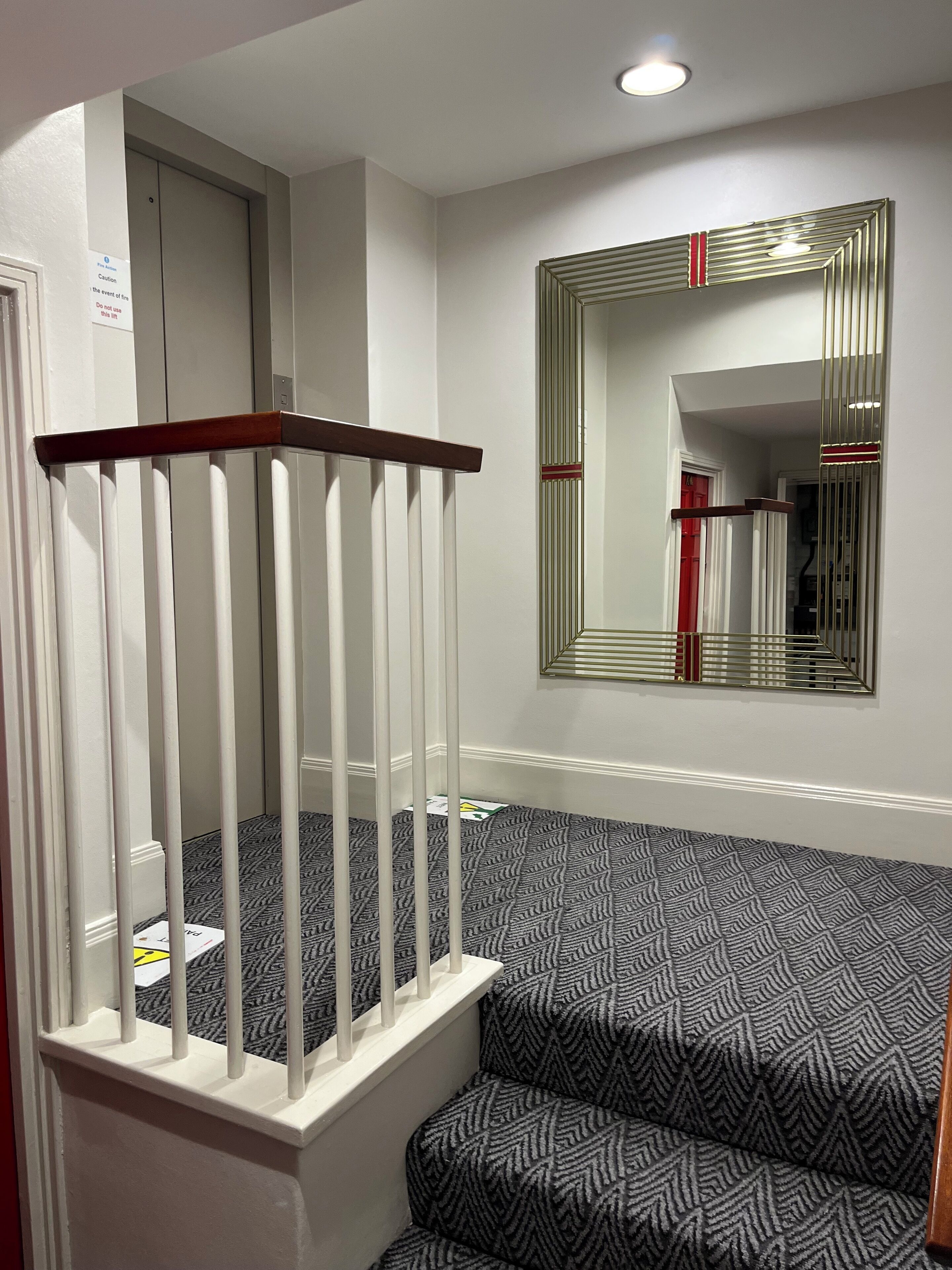 Un escalier recouvert d’une moquette à motifs, doté d’une main courante en bois et agrémenté d’un miroir fixé au mur.