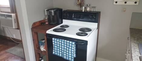 Una cocina con estufa blanca, cafetera y repisa de madera con frascos.