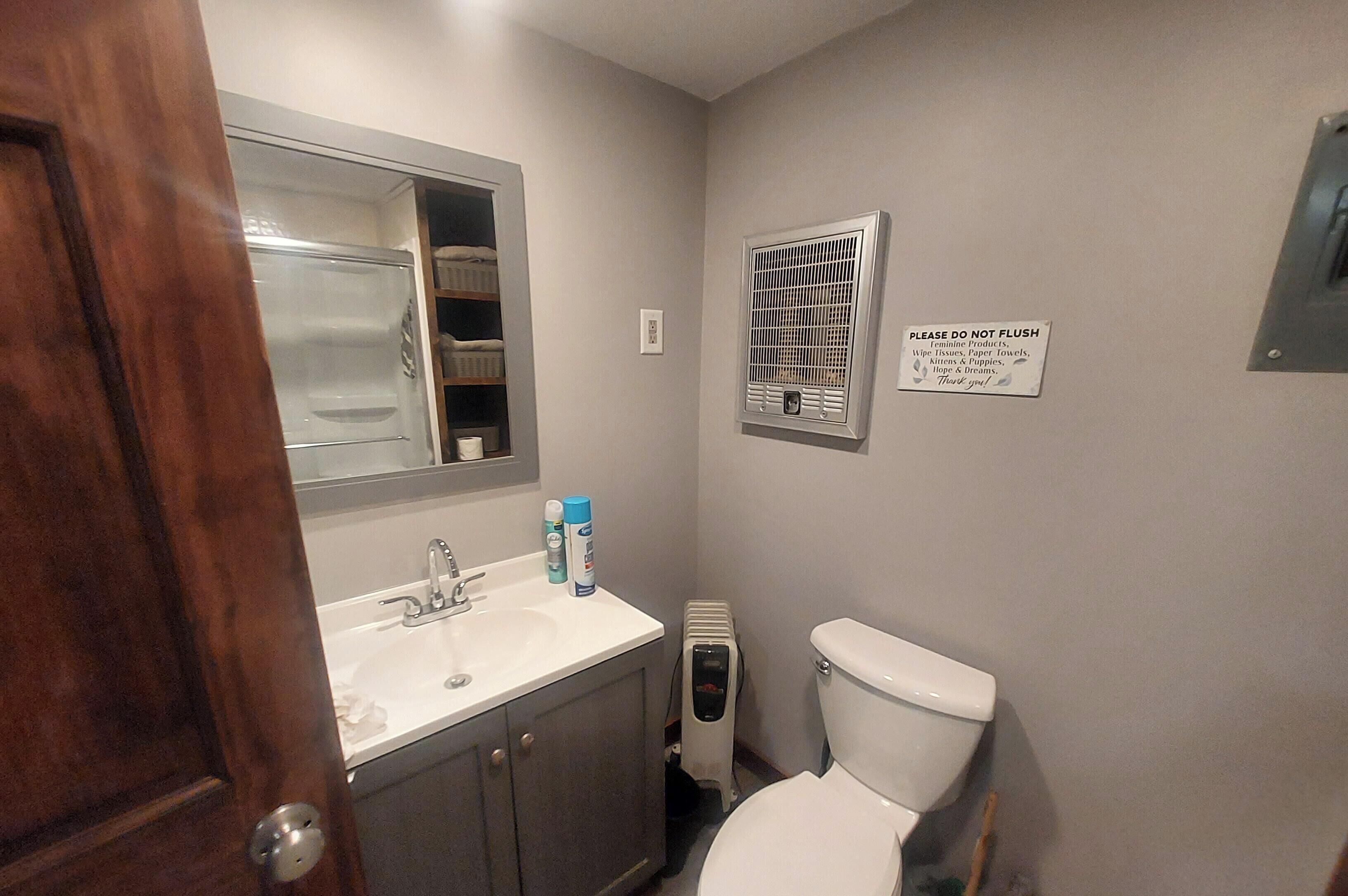 Une salle de bain équipée d’un lavabo, de toilettes et d’un sèche-mains. Un panneau est affiché sur le mur et un miroir se trouve au-dessus du lavabo.