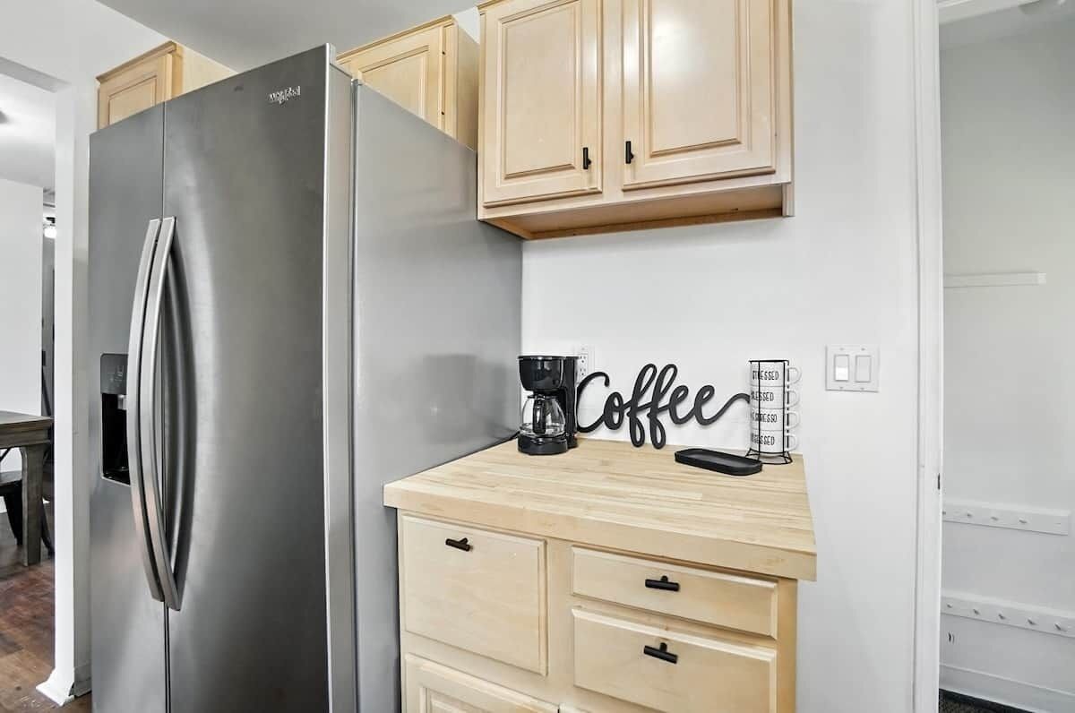 A kitchen with a stainless steel refrigerator, wooden cabinets, a coffee station, and a wall-mounted coffee sign.