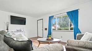 Ein modernes Wohnzimmer mit einem Flachbildfernseher, einem runden Couchtisch und zwei grauen Sofas.