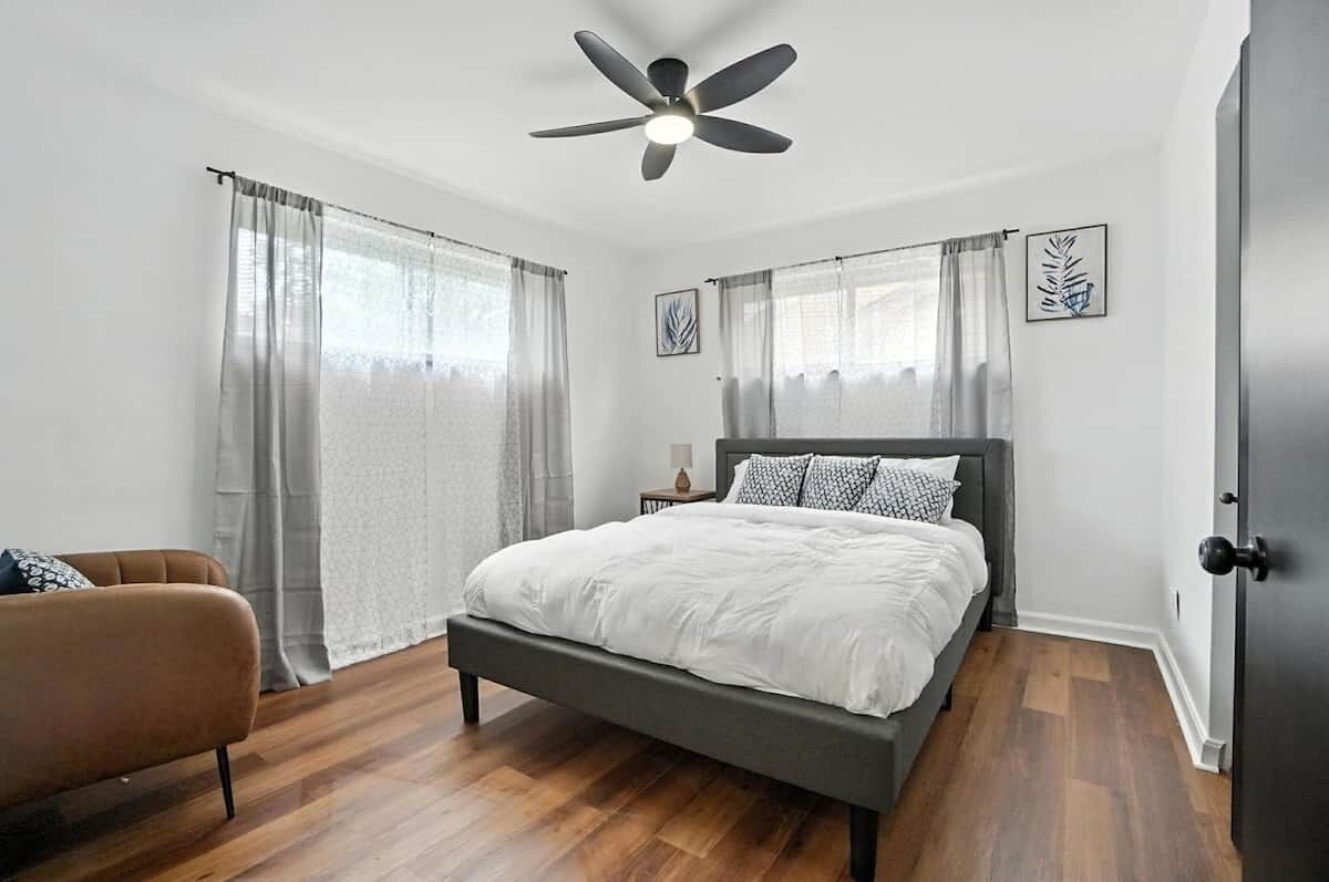 A bedroom with a bed, a ceiling fan, a nightstand, a lamp, and a door.