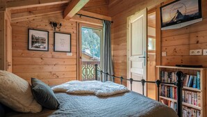 Ein gemütliches Schlafzimmer in einer Holzhütte, mit einem Bett, einem Bücherregal, einem gerahmten Bild und einem an der Wand montierten Fernseher.