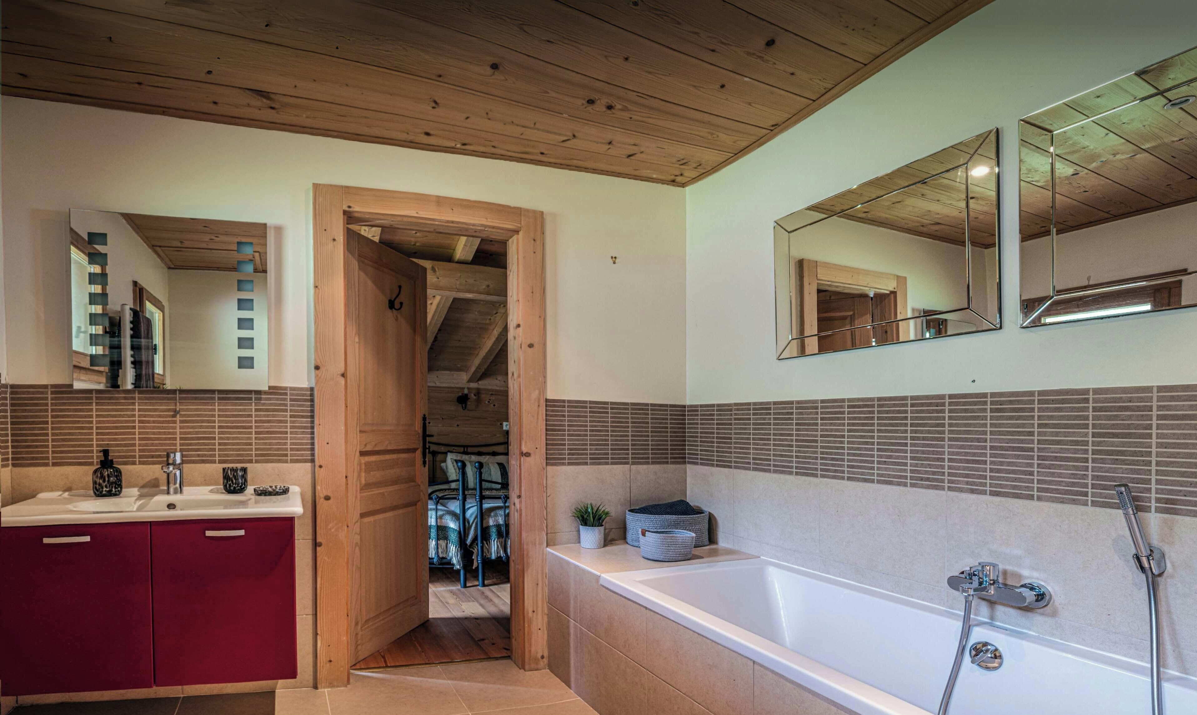 Une salle de bain avec un plafond en bois, un grand miroir, une baignoire et un meuble rouge.