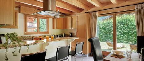 Una cocina moderna con vigas de madera, un comedor con taburetes de bar y vistas al exterior.