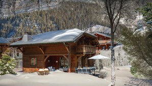 Eine Holzhütte mit Balkon, umgeben von schneebedeckten Bäumen und Bergen.
