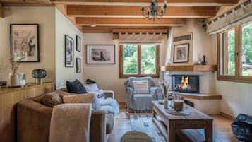 A cozy living room with a fireplace, wooden beams, and a large window with a view of trees.