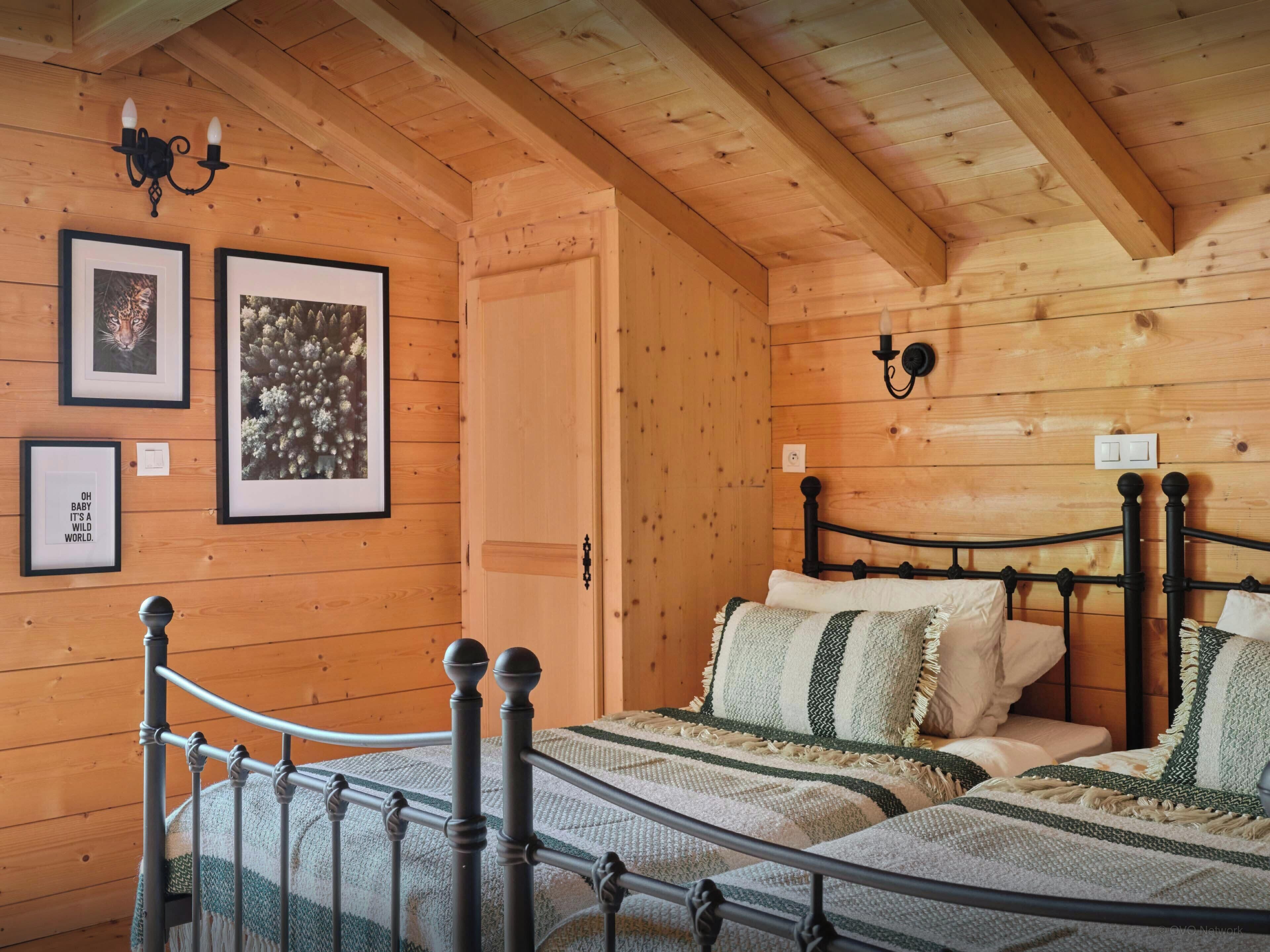 Una habitación de cabaña de madera con cama, cuadros enmarcados y un candelabro.