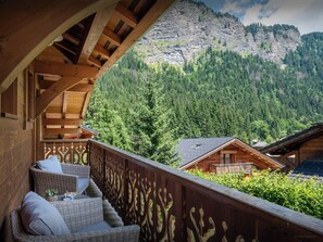 Un balcón de madera con muebles de mimbre, con vistas a un paisaje montañoso con bosques densos.