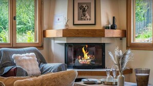 Ein gemütliches Wohnzimmer mit Kamin, einem Bild von einem Hund im Bilderrahmen und einem Fenster mit Blick ins Grüne.