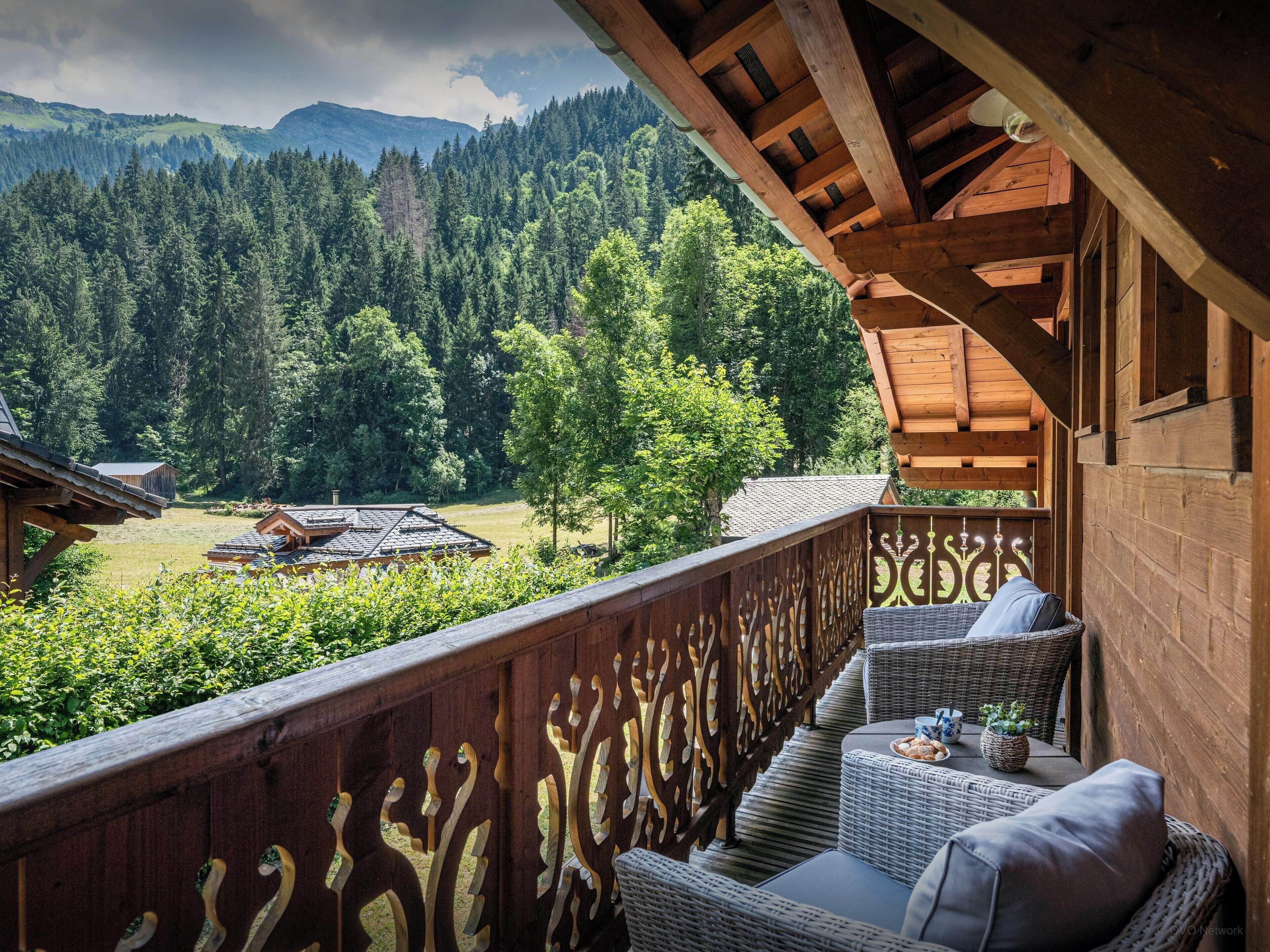 A wooden balcony with wicker furniture and a view of a forested valley.