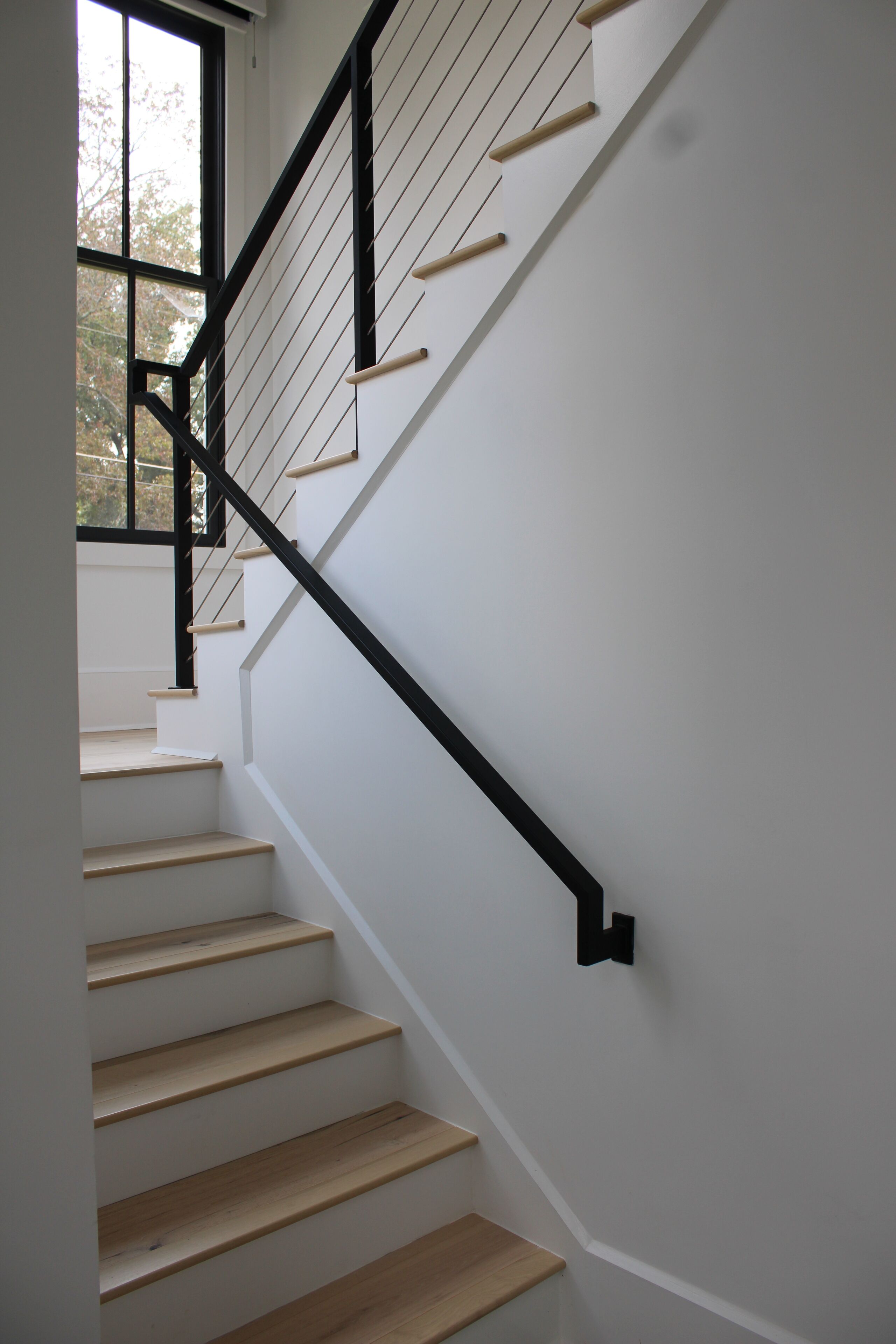 Eine Treppe mit Holzbalken und schwarzen Geländern, die zu einer oberen Etage führt.