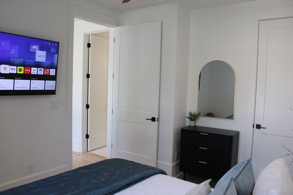 A modern bedroom with a bed, a dresser, a mirror, and a TV displaying a home entertainment system.