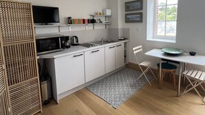 A modern kitchen with white cabinets, a microwave, a coffee maker, and a sink. There is a dining table with chairs and a window providing natural light. - Two-room apartment in the Les Mielles neighborhood (ST CAST LE GUILDO)