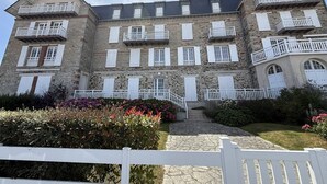 A multi-story stone building with balconies, a stone staircase, and a white picket fence. - Two-room apartment in the Les Mielles neighborhood (ST CAST LE GUILDO)