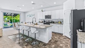 A modern kitchen with white cabinets, a granite countertop, and a central island with bar stools. - 11 Beds,Pool table,Ping Pong,Volleyball+Basketball (Coachella)
