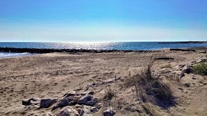 Een zandstrand met rotsformaties en schaarse begroeiing.
