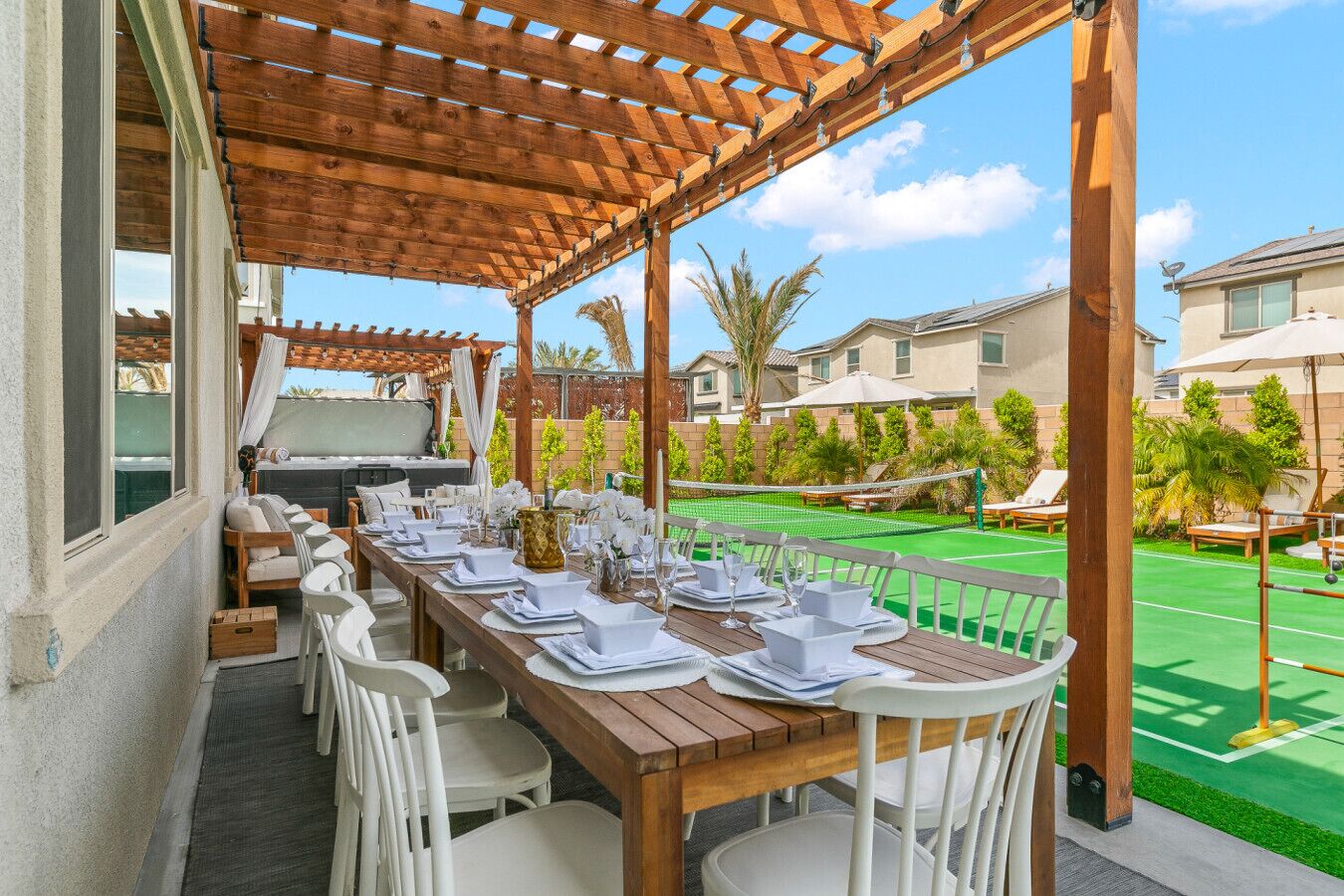 Un área de comedor al aire libre con una pérgola de madera, una mesa de billar y una cancha de tenis al fondo.