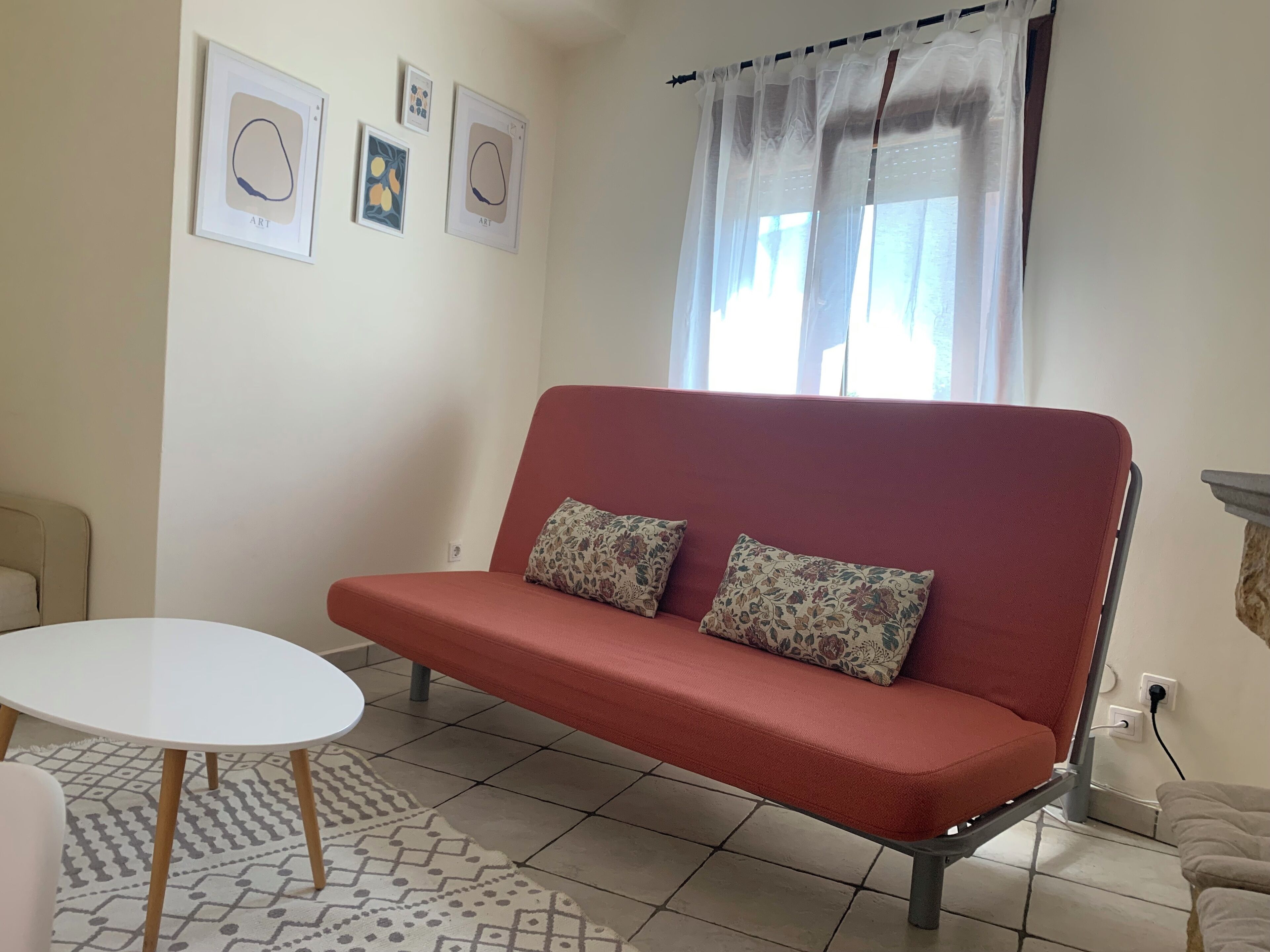 Ein Wohnzimmer mit einem roten Sofa, einem weißen runden Tisch, einem gemusterten Teppich und Kunstwerken an der Wand.