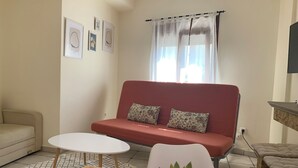 Un salon avec un canapé rouge, une table blanche, un divan beige et une plante en pot.