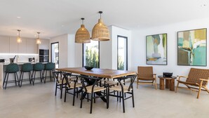 Una cocina moderna con una mesa de comedor de madera, taburetes de bar y lámparas colgantes.
