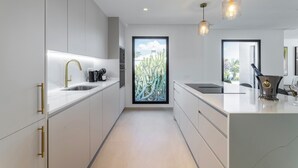 Una cocina moderna con armarios blancos, detalles dorados, un ventanal con vista a un cactus y luminarias colgantes.