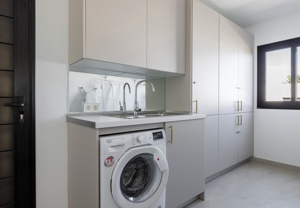 A compact laundry area with a washing machine, a sink, and a window. - BELLAGIO by Buenavilla | Luxury Retreat with Private Heated Pool (Playa Blanca)