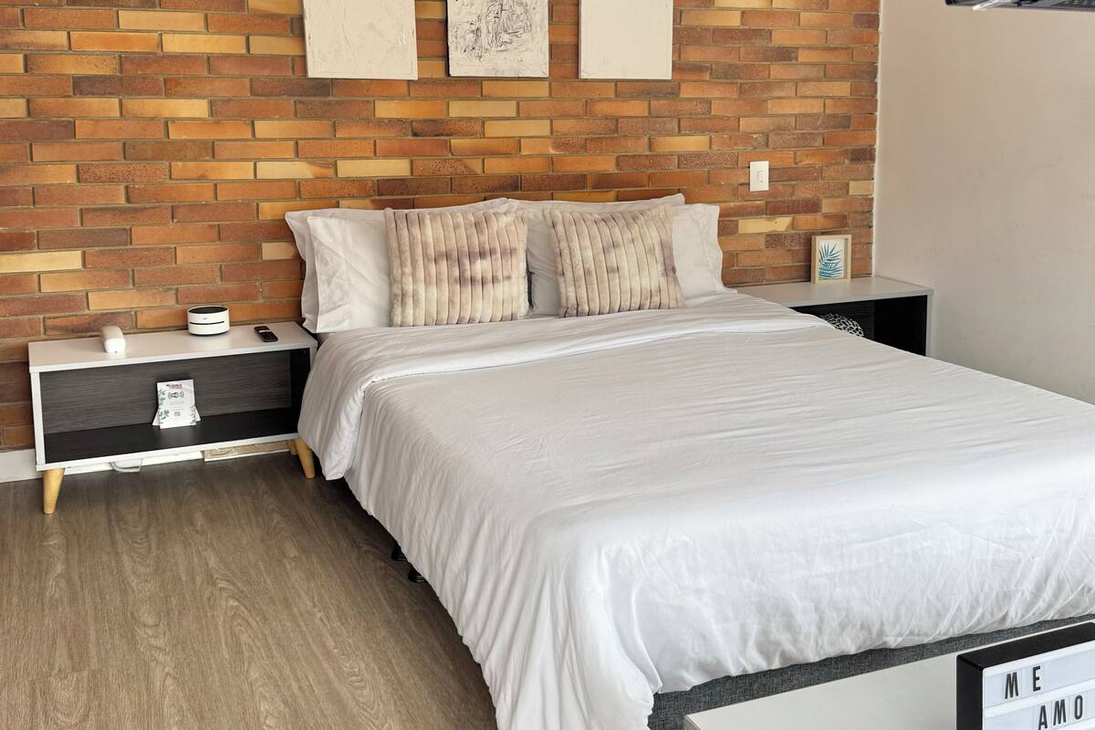 A modern bedroom with a brick-patterned headboard, a white bed, and a bedside table with a lamp.