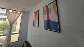 A room with a window, a curtain, and two framed artworks on the wall.