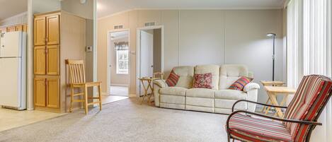 A living room with a beige sofa, a striped armchair, a wooden cabinet, and a ceiling fan.