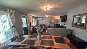 A dining area with a wooden table and chairs, a sofa, a TV, and a clock on the wall.