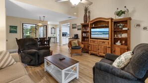 Een ruime woonkamer met een grote televisie, comfortabele zithoek en uitzicht op de oceaan.