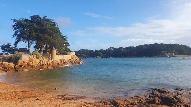 Un paisaje costero con una costa rocosa, una pequeña torre y una colina boscosa al fondo.