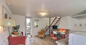 A modern living room with a staircase, a dining area with red chairs, and a fireplace.