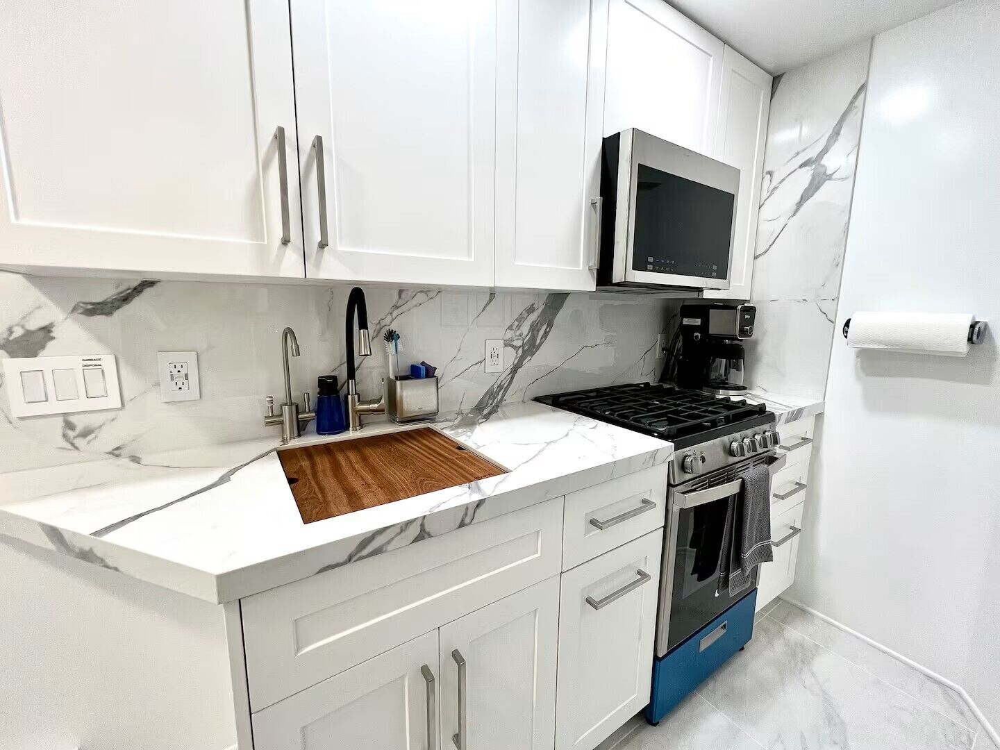 A modern kitchen with white cabinets, a built-in microwave, a stove, and a sink with a wooden countertop.